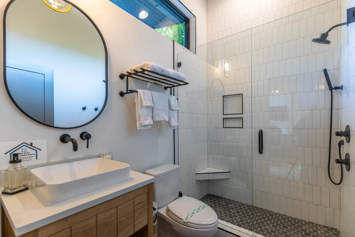 A stylish, modern bathroom with a large circular mirror above a wooden vanity, a walk-in shower with contemporary fixtures, and neatly folded white towels. The clean lines and soothing palette create a spa-like atmosphere.