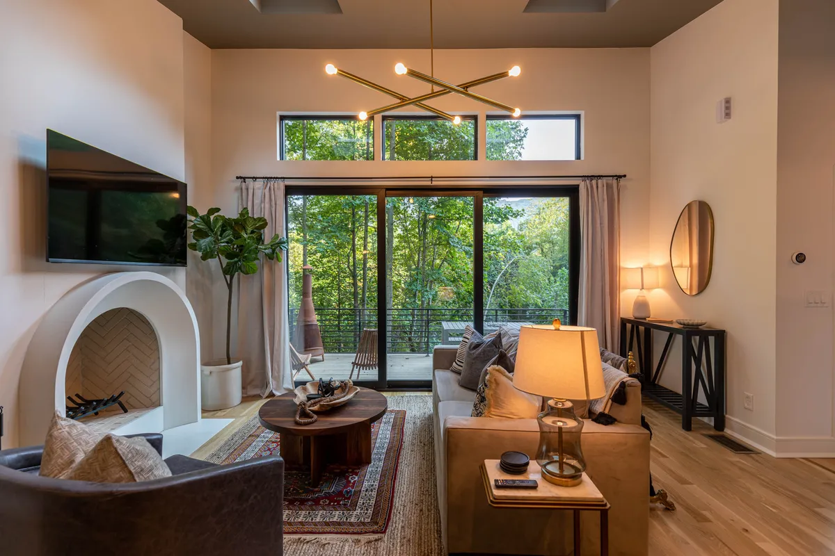 A cozy and stylish great room, anchored by a stunning fireplace. Large windows frame the surrounding greenery and let in abundant natural light. The comfortable sofa and coffee table create an inviting space for relaxing, reading, or enjoying a fire. The room's open layout and expansive glazing blur the boundaries between indoors and the forest beyond.