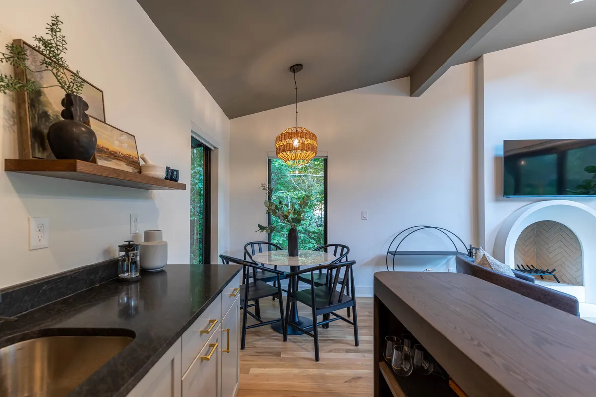 A cozy dining area featuring a wooden table beneath a modern pendant light, positioned beside a window that offers a peaceful view of the outdoors. The setting is intimate and versatile, suitable for enjoying a morning coffee, casual meals, or taking a reflective break while gazing at the scenery.