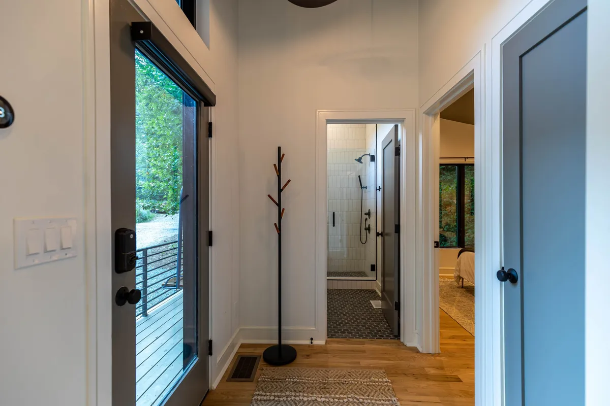 This image captures the welcoming entryway of Little Bear Escape, highlighting the front door, a coatrack for hanging outdoor gear, and a glimpse of the shower area beyond. The inviting atmosphere suggests a cozy return home after exploring nearby attractions or outdoor adventures.