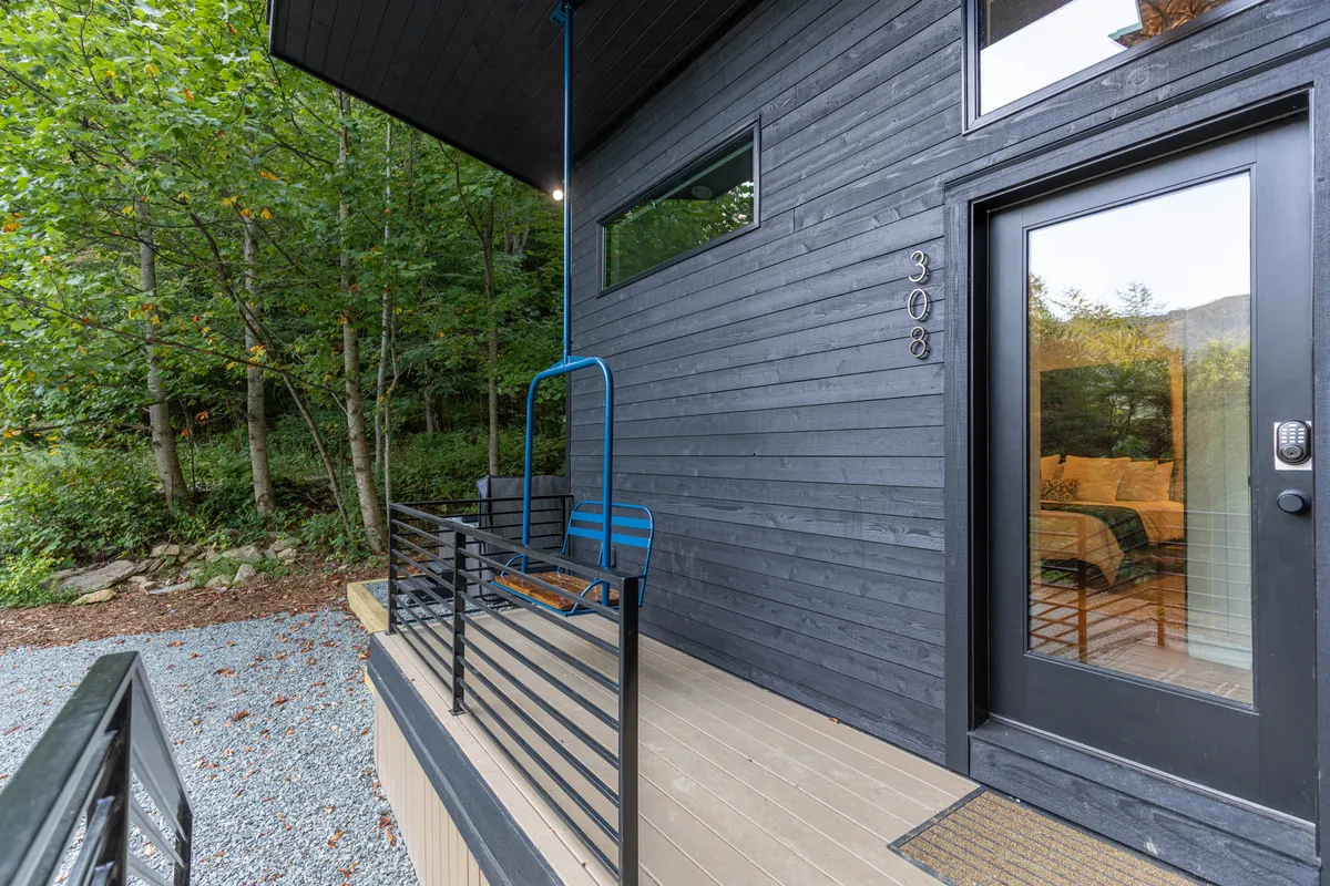 A modern deck entryway with a hanging chair swing, surrounded by lush greenery. The area is peaceful and inviting, illustrating how guests can relax and enjoy mountain air. The unique ski lift swing feature is represented by the hanging chair, suggesting playful and whimsical seating options on the deck.