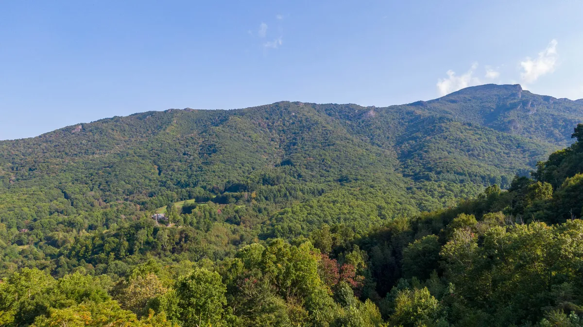 This image captures a sweeping mountain range set against a blue sky, framed by lush green trees. It evokes the natural beauty and panoramic views central to the region, embodying the romantic, outdoorsy spirit highlighted in the section.